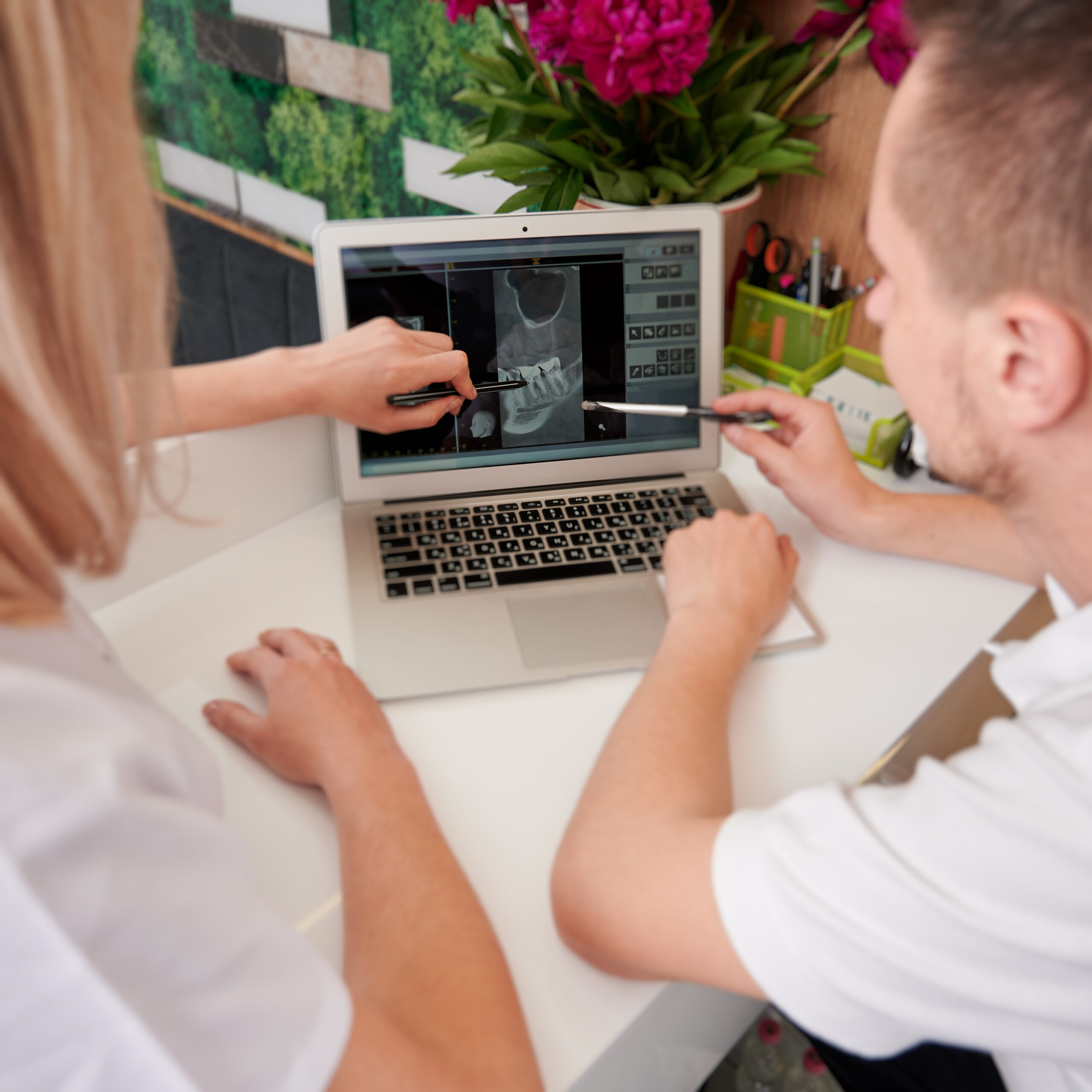 Young female dentist with assistant analyzing x ray image on pc in clinic